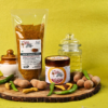 Tamarind Green Chilli Pickle (Pachi Chinthakaya Thokku) in pouch and jar packaging with raw tamarind, green chillies, and turmeric on a wooden platter.